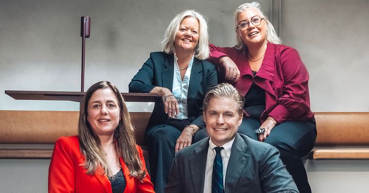 Alt-text: Fyra personer sitter och står i en gruppbild, klädda i formella kläder.