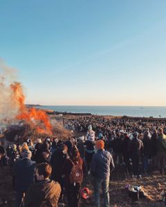Människor som samlats vid en stor påskbrasa intill havet.