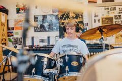 Leende elev i blå tröja och hörlurar som sitter vid trummor och spelar