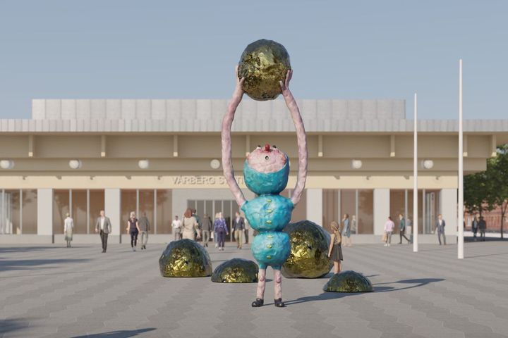 En stor, färgglad skulptur med flera runda segment står utomhus. Den håller upp en guldfärgad boll ovanför huvudet, och liknande bollar ligger på marken runt omkring. Människor går förbi i bakgrunden.