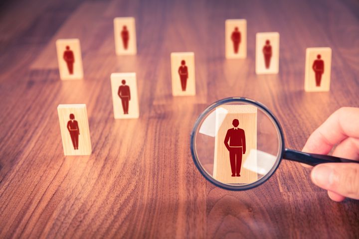 Symbolisk bild för en befolkningsundersökning där ett förstoringsglas hålls framför en dominobricka med bilden av en stiliserad person. Fler brickor syns också i bilden.