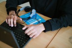 Person skriver på en bärbar dator och har hörlurar bredvid sig på ett bord.