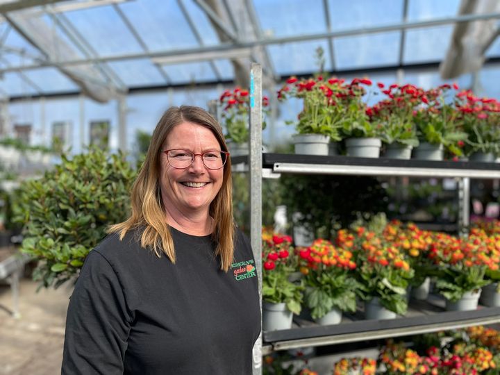 Kvinna i ett växthus med blommor i bakgrunden.