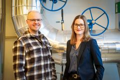 Man och kvinna som står framför fjärrvärmerör och tittar in i kameran.