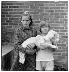 Svartvit bild av två barn som tillsammans håller en vit hund i famnen.