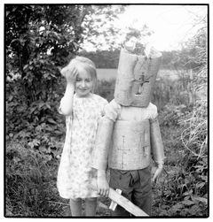 Svartvit bild av två barn varav ett har en kostym gjord av näver av och håller ett träsvärd.