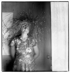 Svartvit bild av kvinna i blommig klänning och blomsterkvast på huvudet.