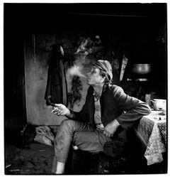 Svartvit bild av sittande man som röker i kök.