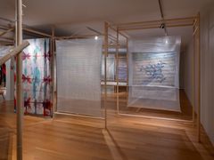 Konstinstallation med transparenta tyger upphängda i en träställning, med abstrakta motiv och färgnyanser i blått och rött.