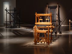 Museiutställning med vävstolar och uppspända snören under svag belysning.