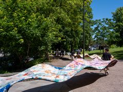 En utomhusinstallation med färgglada vågformade skulpturer, uppställda i en park. Besökare promenerar längs verket.