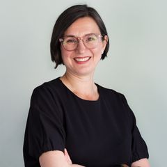 porträttbild av kvinna i svart t-shirt, ljusa glasögon och mörk page-frisyr.