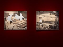 Två inramade bilder på en röd vägg, avbildar silhuetter av personer vid maskiner.