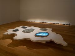 En skulptur på ett golv som liknar en vattenyta med flera stenar placerade på den.