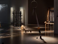 Installation med skulpturer, ljuskällor och textilier projicerar skuggor på golvet i ett mörkt rum.