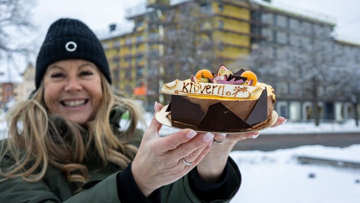 "Kvinna i vinterkläder håller en tårta med dekorationer utomhus."