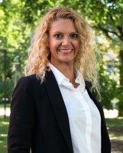 Kvinna i vit skjorta och svart kavaj ler och tittar in i kameran