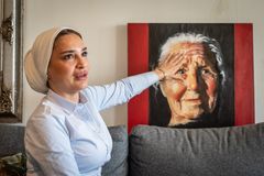 Kvinna sitter i en soffa och rör vid ett porträtt av en äldre kvinna.