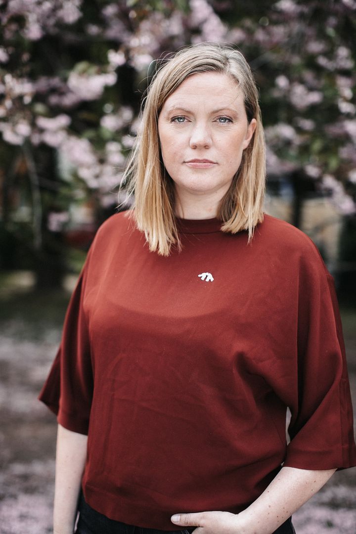 Kvinna med röd tröja med vit pin från Svenska Freds står framför körsbärsträd och ser in i kameran