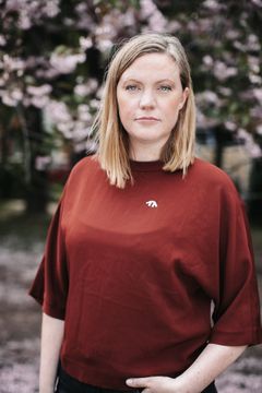 Kvinna med röd tröja med vit pin från Svenska Freds står framför körsbärsträd och ser in i kameran