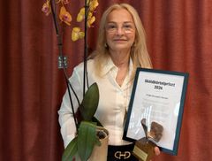 Frida håller en orkidé, en fjärilsstatyett och ett diplom med texten "Sköldkörtelpriset 2026".