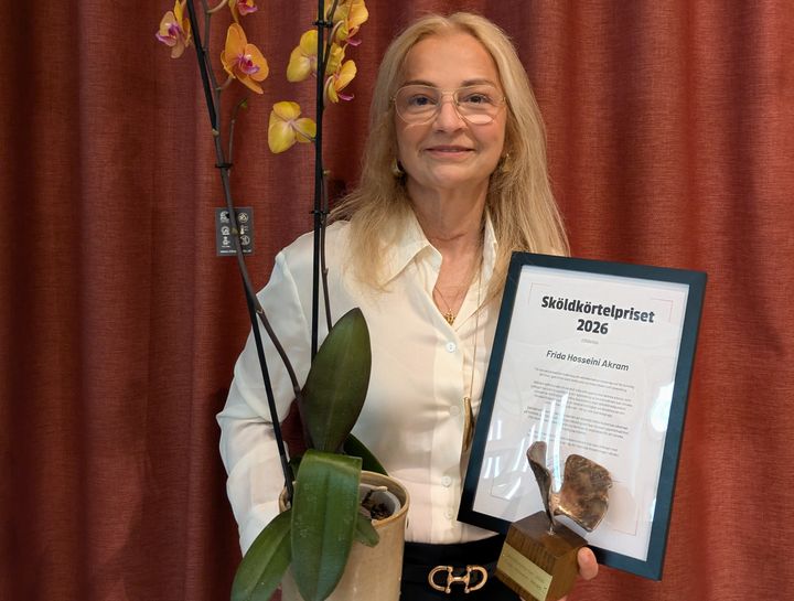 Frida håller en orkidé, en fjärilsstatyett och ett diplom med texten "Sköldkörtelpriset 2026".