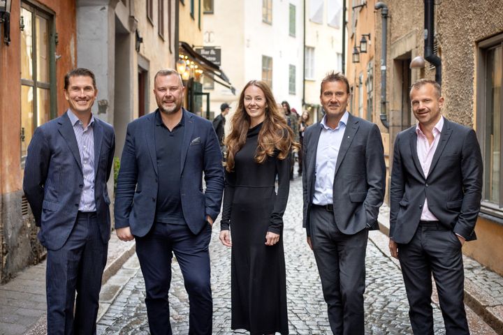 Fem personer står leende på en kullerstensgata.