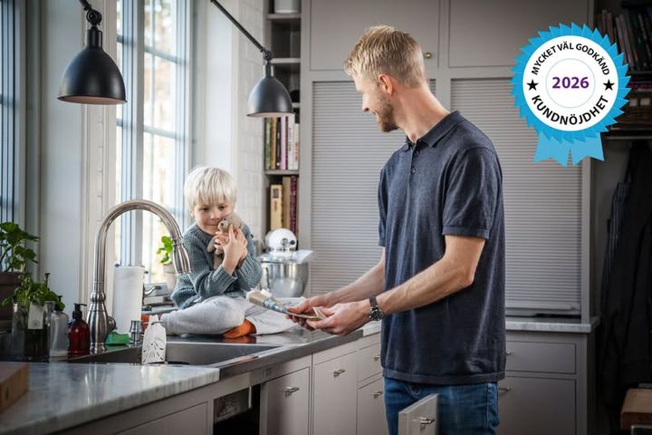 Far och son i köket, sonen sitter på bänken och äter, pappan serverar. Bakgrunden visar köksinredning och en stämpel med "Mycket väl godkänd 2026 Kundnöjdhet".