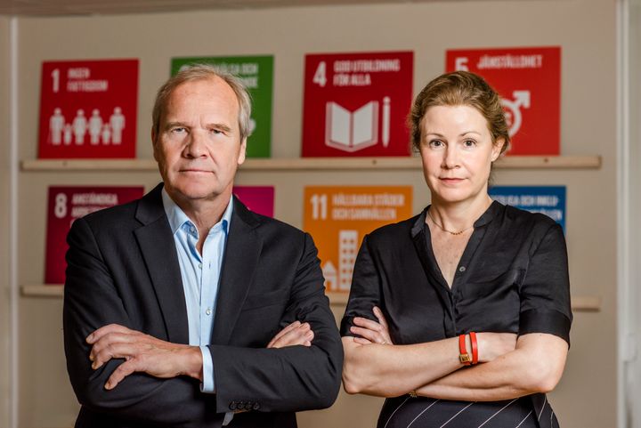 Anders Lago, förbundsordförande för Riksförbundet FUB, och Christina Heilborn, förbundssekreterare för Riksförbundet FUB, står bredvid varandra med armarna korsade över bröstet. De står framför en vägg med färgglada skyltar av de globala målen för hållbarhet i Agenda 2030.