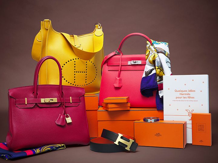Lyxiga handväskor i rött och gult med Hermès-märkta förpackningar och accessoarer i bakgrunden.