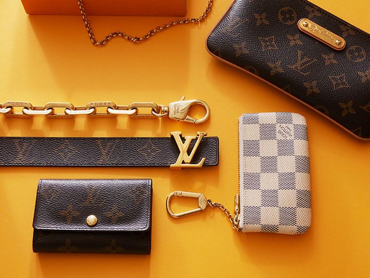 Olika Louis Vuitton-accessoarer mot en gul bakgrund, inklusive plånböcker, nyckelring och kedjor.
