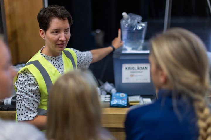 En person med gul väst står framför en grupp, pekar på en låda märkt "Krislådan".