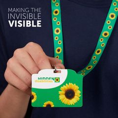 En person håller i ett grönt nyckelband med solrosdesign och en bricka som signalerar osynliga funktionsnedsättningar.
