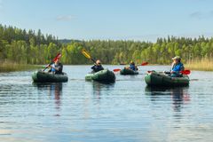 En grupp paddlar packraft på lugnt vatten med skog i bakgrunden