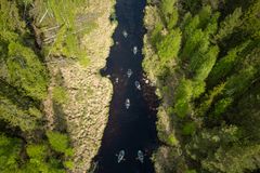 Drönarbild av en grupp som paddlar packraft längs en smal, skogskantad å