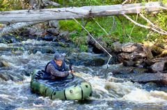 Marcus Eldh paddlar en grön packraft genom en mindre fors i ett skogsvattendrag