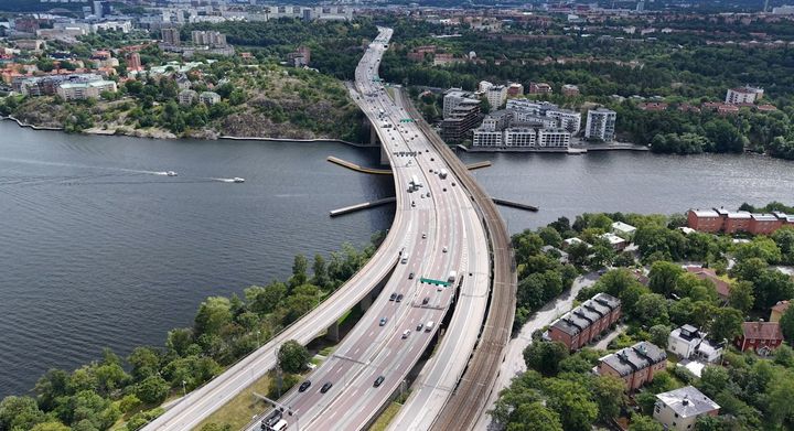 Flygbild över Essingeleden med trafik, omgiven av vatten och grönområden.