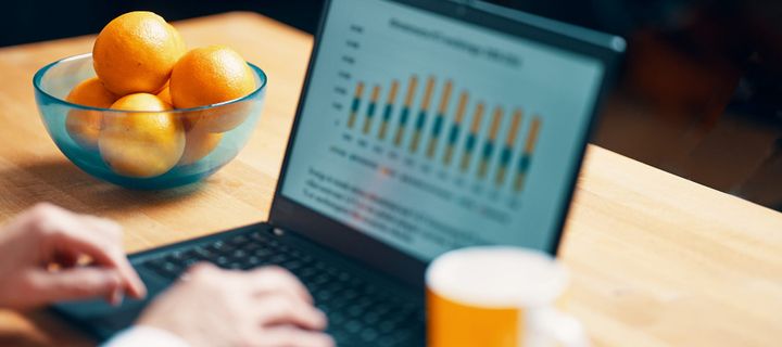 arbete på laptop vid skrivbord, skål med apelsiner på bordet