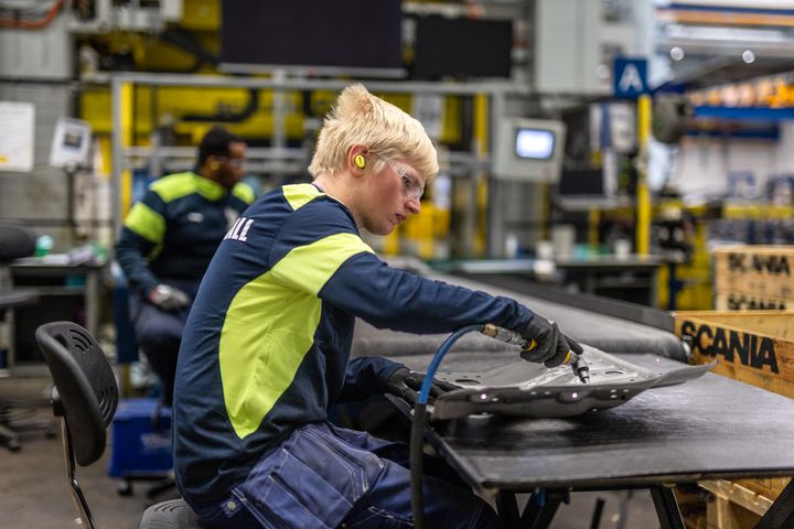 En man i arbetskläder bearbetar material på en arbetsstation i en fabrik.