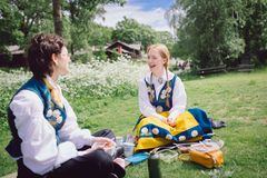 Tow girls dressed in Swedish national costume enjoying a picnic at Skansen.